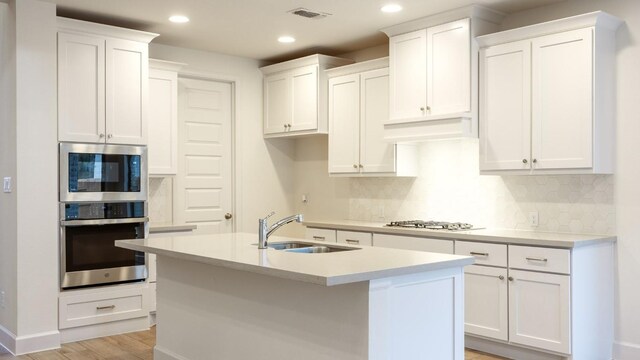 kitchen featuring sink, tasteful backsplash, appliances with stainless steel finishes, an island with sink, and white cabinets