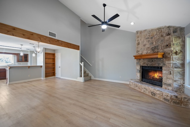 unfurnished living room featuring light hardwood / wood-style flooring, high vaulted ceiling, ceiling fan with notable chandelier, and a fireplace