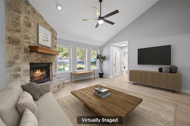 living room featuring high vaulted ceiling, ceiling fan, light hardwood / wood-style floors, and a stone fireplace