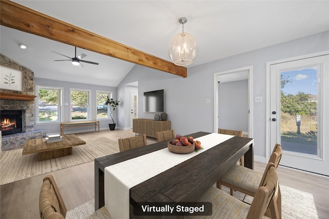 dining room featuring a stone fireplace, ceiling fan with notable chandelier, lofted ceiling with beams, and light hardwood / wood-style flooring