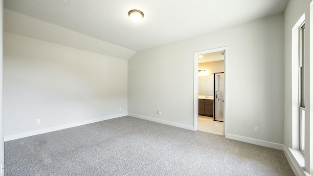 unfurnished bedroom with connected bathroom, light colored carpet, and lofted ceiling