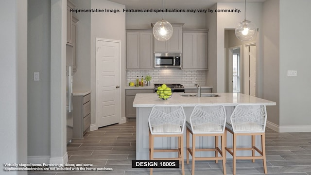 kitchen with gray cabinetry, a kitchen island with sink, sink, and appliances with stainless steel finishes