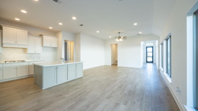 kitchen featuring a kitchen island with sink, decorative backsplash, ceiling fan, light hardwood / wood-style floors, and white cabinetry