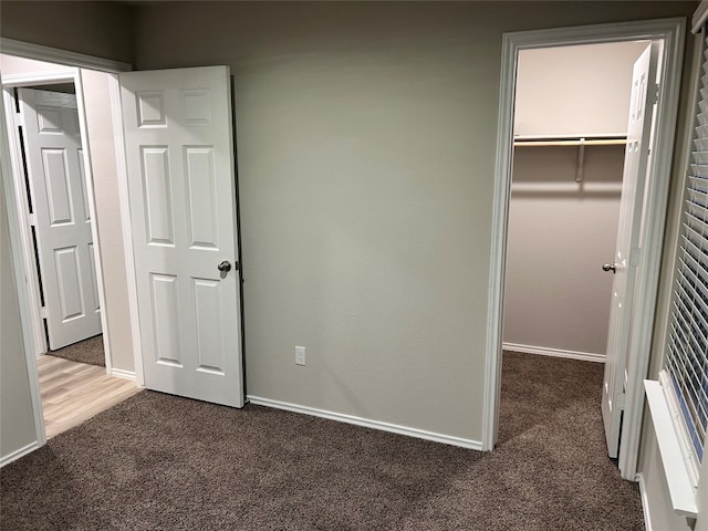 unfurnished bedroom featuring dark colored carpet, a closet, and a spacious closet