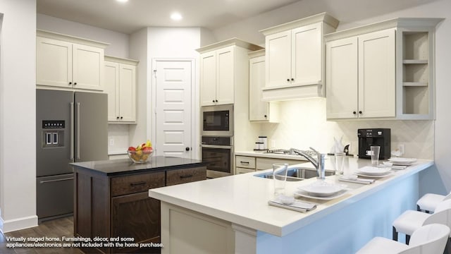 176 Plumbago Loop, Bastrop, TX 78602 - kitchen with stainless steel appliances, a peninsula, a center island, dark wood finished floors, and a breakfast bar