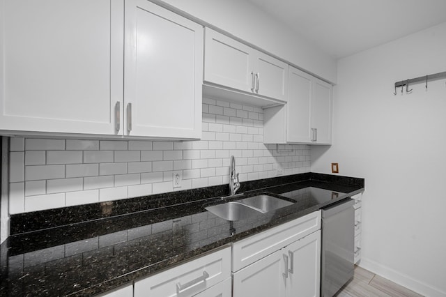 kitchen with white cabinetry, stainless steel dishwasher, sink, and dark stone countertops