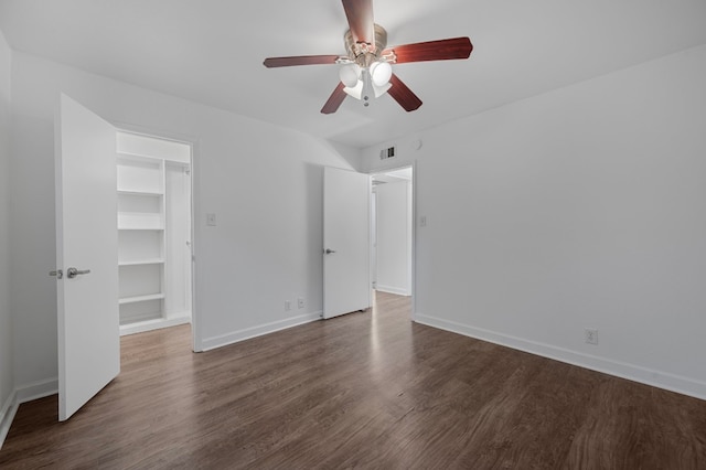 unfurnished bedroom with dark hardwood / wood-style flooring, a closet, a walk in closet, and ceiling fan