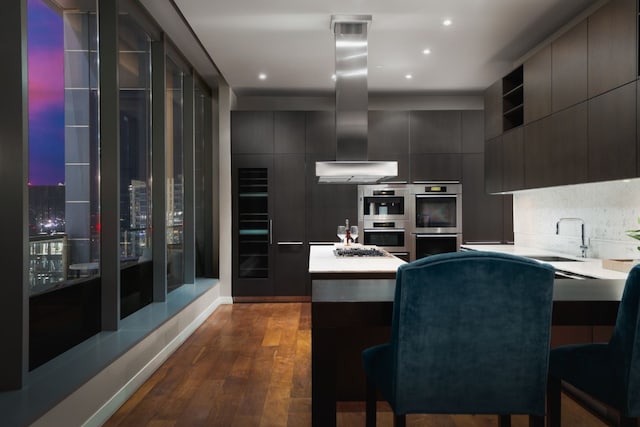 kitchen with stainless steel appliances, range hood, dark hardwood / wood-style floors, sink, and a kitchen breakfast bar