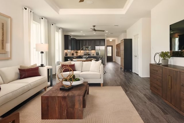 living room with dark wood-type flooring, a tray ceiling, and ceiling fan