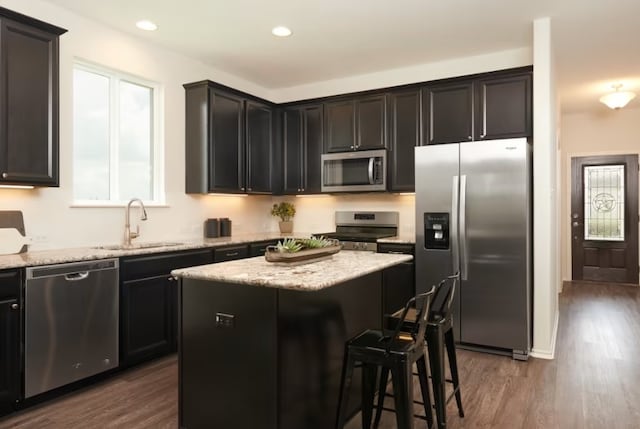 kitchen featuring light stone counters, appliances with stainless steel finishes, dark hardwood / wood-style floors, sink, and a center island