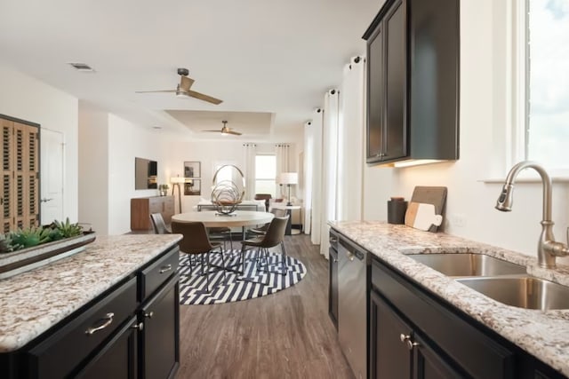 kitchen featuring dark wood-type flooring, light stone countertops, sink, dishwasher, and a tray ceiling