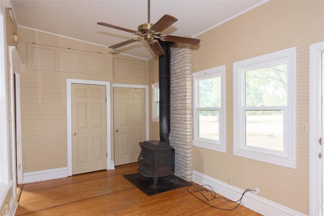 unfurnished living room with a wood stove, light wood-style floors, ceiling fan, and baseboards