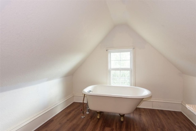 bathroom featuring a soaking tub, vaulted ceiling, baseboards, and wood finished floors