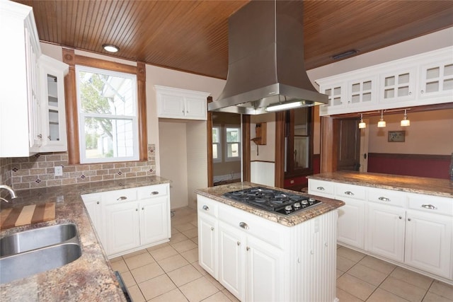 kitchen featuring island range hood, a sink, decorative backsplash, glass insert cabinets, and stainless steel gas stovetop