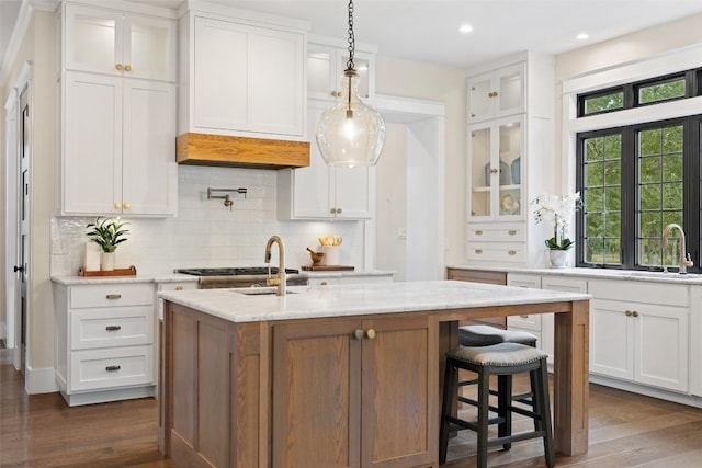 kitchen with a center island with sink, dark hardwood / wood-style floors, decorative light fixtures, light stone counters, and white cabinetry