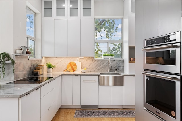 kitchen with black electric cooktop, light stone countertops, white cabinetry, and double oven