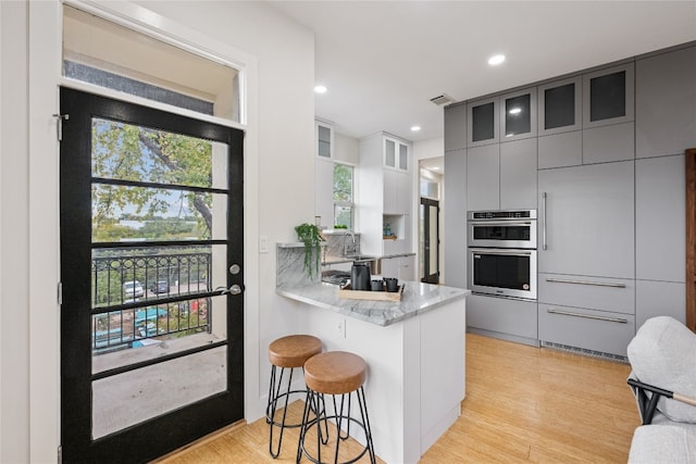 kitchen featuring a kitchen breakfast bar, kitchen peninsula, double oven, and light hardwood / wood-style floors