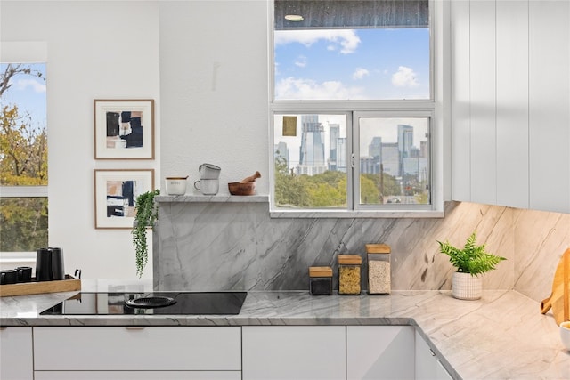 kitchen featuring black electric cooktop, white cabinetry, light stone counters, and tasteful backsplash