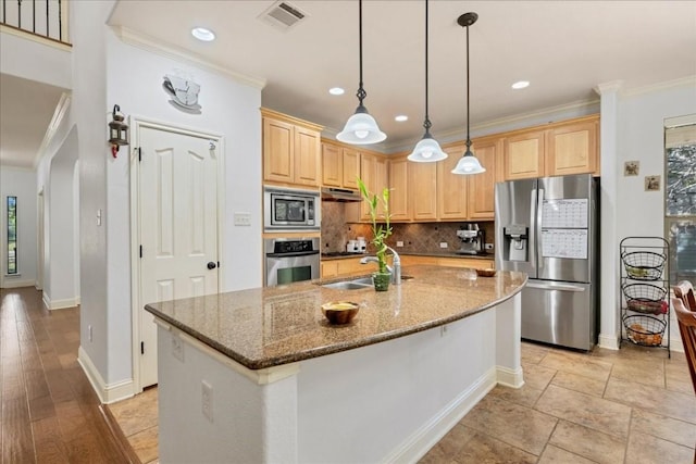 kitchen with light brown cabinets, a center island with sink, stainless steel appliances, and stone counters