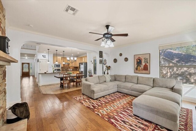 living room with hardwood / wood-style floors, ornamental molding, ceiling fan with notable chandelier, and a fireplace