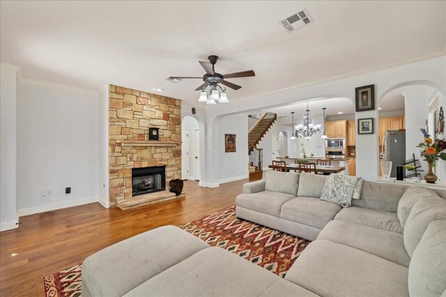 living room featuring crown molding, a fireplace, ceiling fan with notable chandelier, and hardwood / wood-style floors