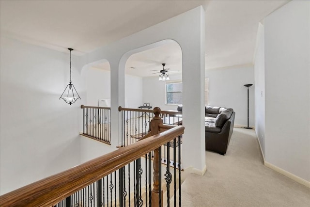 hall with light carpet, arched walkways, an upstairs landing, and baseboards