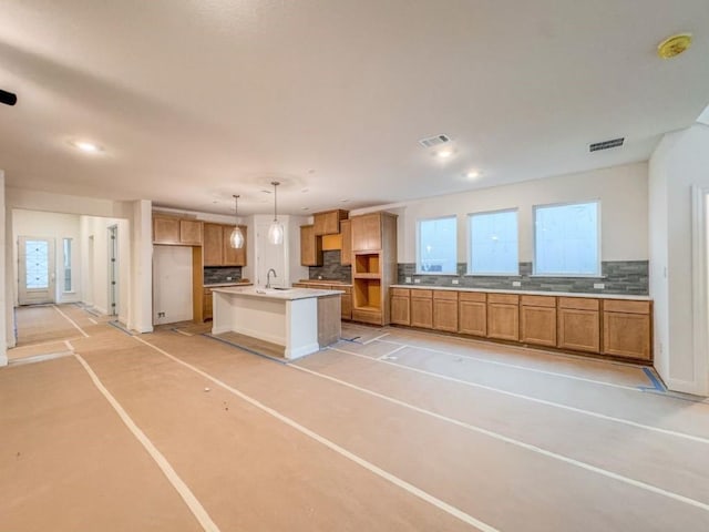 kitchen featuring hanging light fixtures, decorative backsplash, plenty of natural light, and a center island with sink