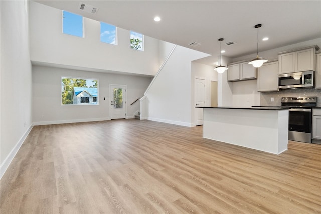 kitchen with stainless steel appliances, backsplash, hanging light fixtures, light hardwood / wood-style flooring, and gray cabinets