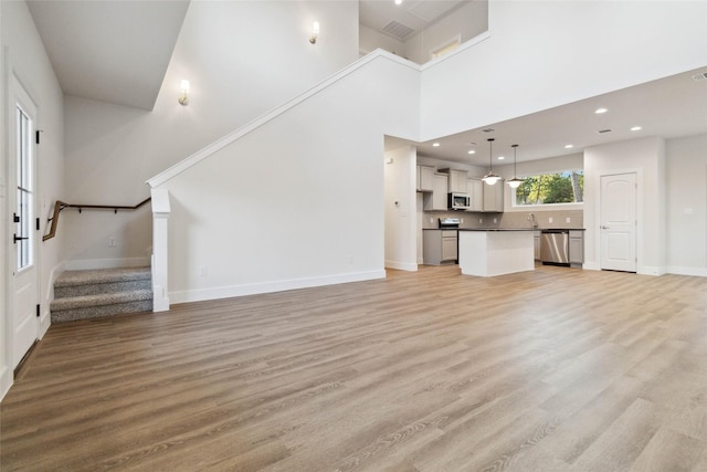 unfurnished living room featuring a high ceiling, sink, and light wood-type flooring