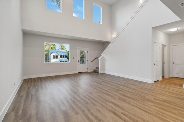 unfurnished living room with a towering ceiling and light wood-type flooring