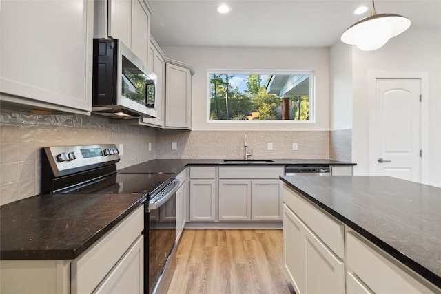 kitchen with sink, decorative light fixtures, appliances with stainless steel finishes, light hardwood / wood-style floors, and decorative backsplash