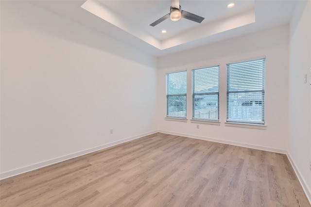 spare room featuring light wood-type flooring, ceiling fan, and a tray ceiling