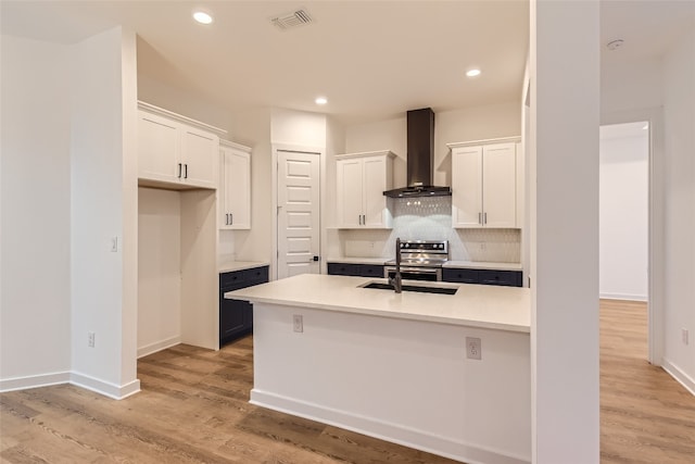 kitchen with stainless steel electric range, light hardwood / wood-style floors, white cabinets, wall chimney exhaust hood, and tasteful backsplash