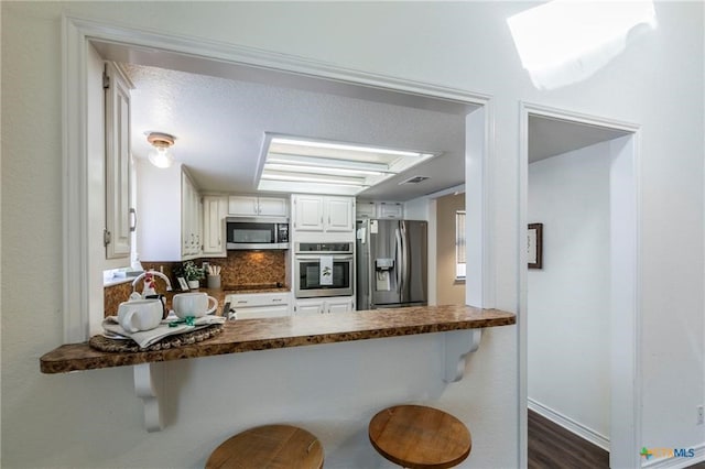 kitchen featuring stainless steel appliances, a kitchen bar, white cabinetry, and tasteful backsplash