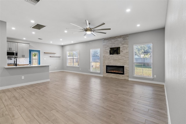 unfurnished living room with light wood-type flooring, sink, ceiling fan, and a fireplace