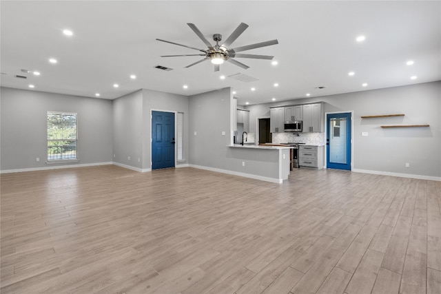 unfurnished living room with light wood-type flooring, ceiling fan, and sink