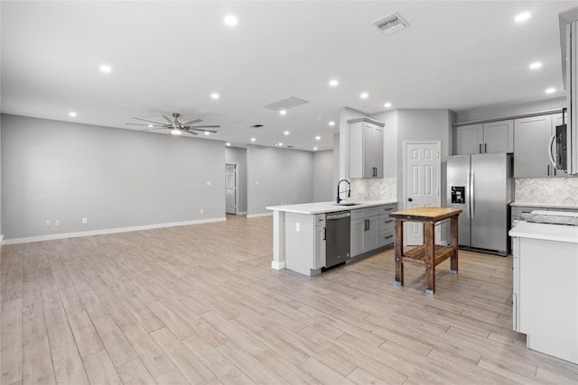 kitchen featuring gray cabinets, light hardwood / wood-style flooring, decorative backsplash, and stainless steel appliances