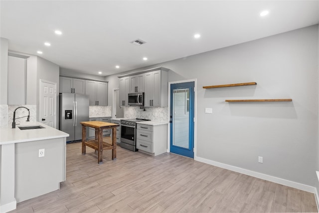 kitchen with decorative backsplash, sink, gray cabinetry, light wood-type flooring, and appliances with stainless steel finishes