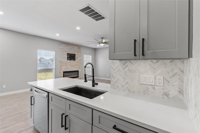 kitchen with stainless steel dishwasher, sink, light wood-type flooring, and gray cabinetry