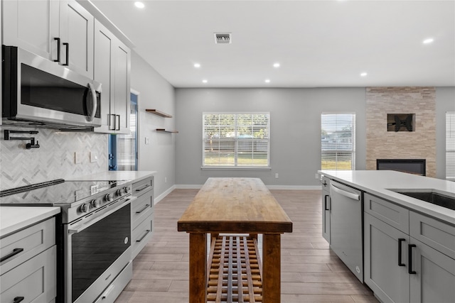 kitchen featuring light hardwood / wood-style floors, tasteful backsplash, gray cabinets, a fireplace, and appliances with stainless steel finishes