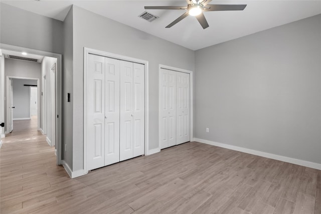 unfurnished bedroom featuring multiple closets, light hardwood / wood-style floors, and ceiling fan