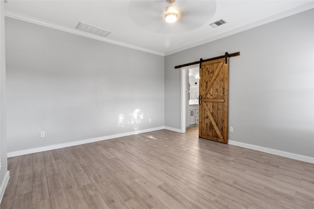 empty room featuring ornamental molding, light hardwood / wood-style floors, and a barn door