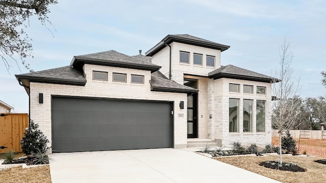 prairie-style house featuring a garage, a shingled roof, fence, and concrete driveway