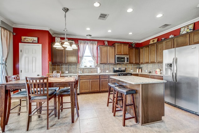 kitchen with ornamental molding, stainless steel appliances, hanging light fixtures, and a kitchen island