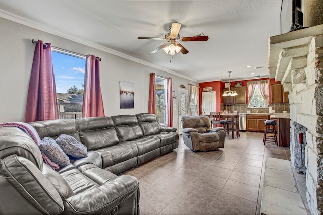 tiled living room featuring a stone fireplace, ornamental molding, and ceiling fan with notable chandelier