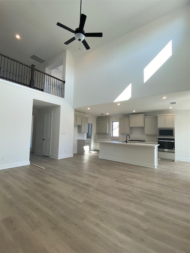 unfurnished living room featuring a towering ceiling, sink, ceiling fan, and light hardwood / wood-style floors