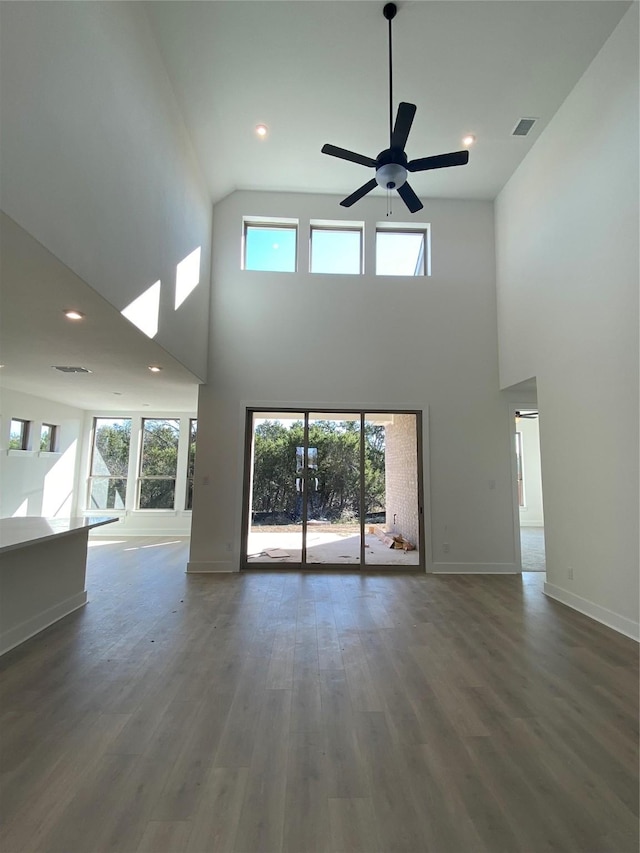 unfurnished living room featuring a healthy amount of sunlight, ceiling fan, dark hardwood / wood-style flooring, and a towering ceiling