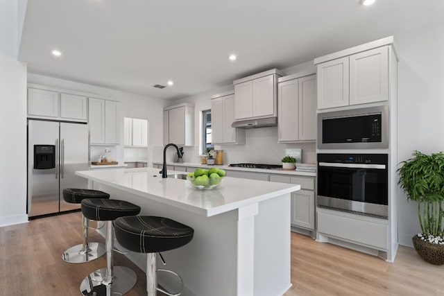 1515 Cardinal Ln, Round Rock, TX 78681 - kitchen featuring appliances with stainless steel finishes, a sink, light countertops, a center island with sink, and a breakfast bar