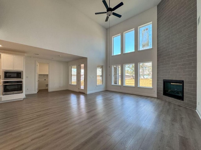 unfurnished living room with a wealth of natural light, a brick fireplace, dark wood-style floors, and ceiling fan