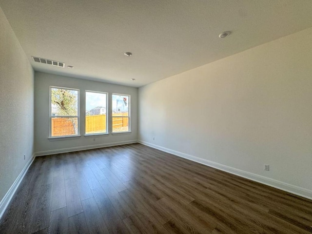 empty room featuring visible vents, dark wood-type flooring, and baseboards